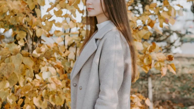 Woman wearing a tailored coat standing among colorful autumn leaves