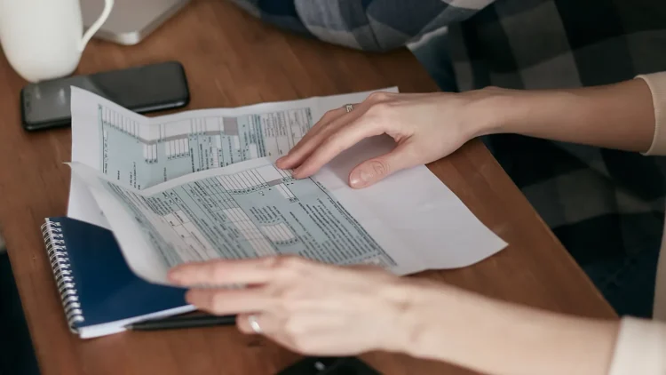 Hands organizing tax forms on a desk next to a calculator and laptop