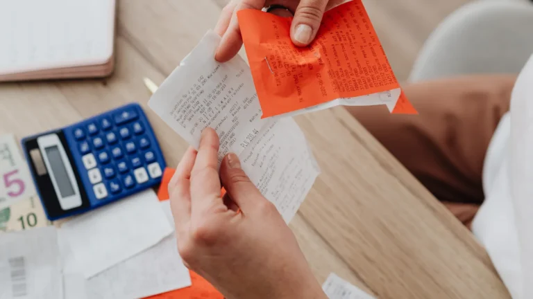 Person organizing receipts and notes with a calculator at a desk