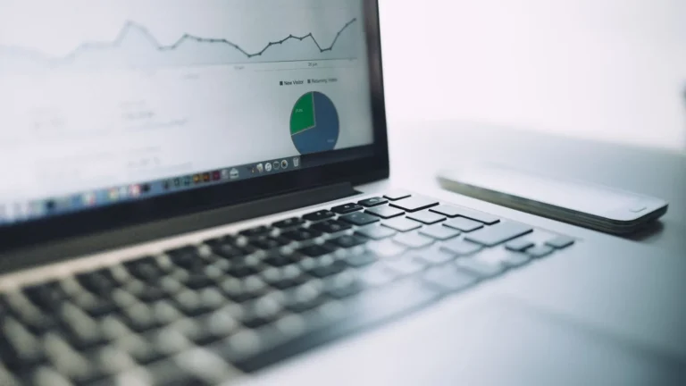 Laptop on a desk showing a pie chart beside a notebook and smartphone