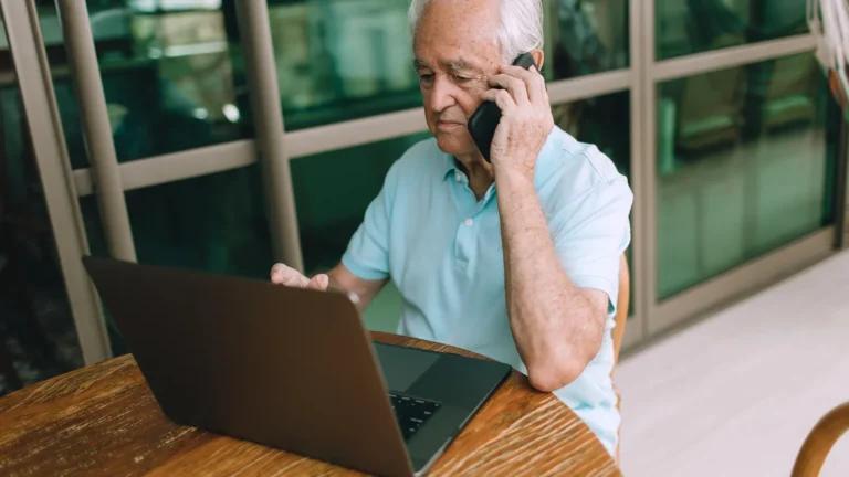 Older man working on a laptop and phone at home while planning retirement income